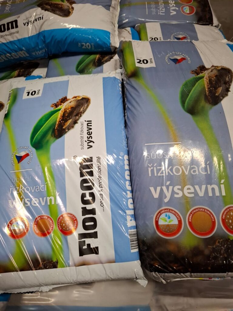 Obrázok zobrazuje balíky substrátu na výsev s označením Florcom, ktoré sú uskladnené v priestore. Každý balík obsahuje informácie o objeme a type substrátu, pričom sú viditeľné aj grafické prvky a logá výrobcu.