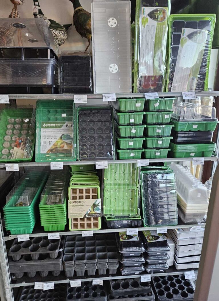 Regály s rôznymi plastovými sadbovými nádobami a traymi na sadenice, zoradené podľa veľkosti a typu, v predajni záhradníckych potrieb.