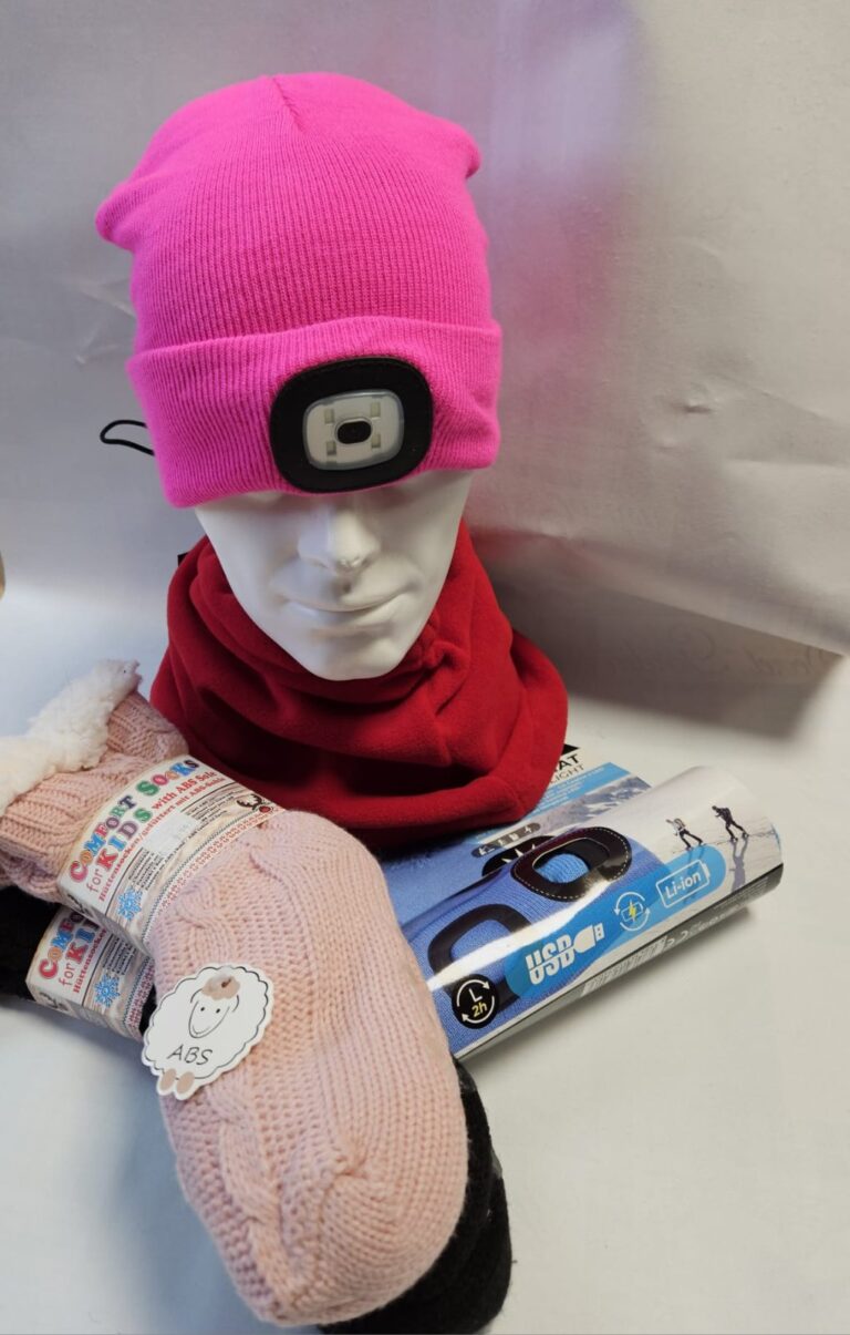 Hlava manekýna s ružovou čiapkou s LED svetlom, červeným šálom a detskými rukavicami v svetloružovej farbe, vedľa balíka so zimným vybavením.