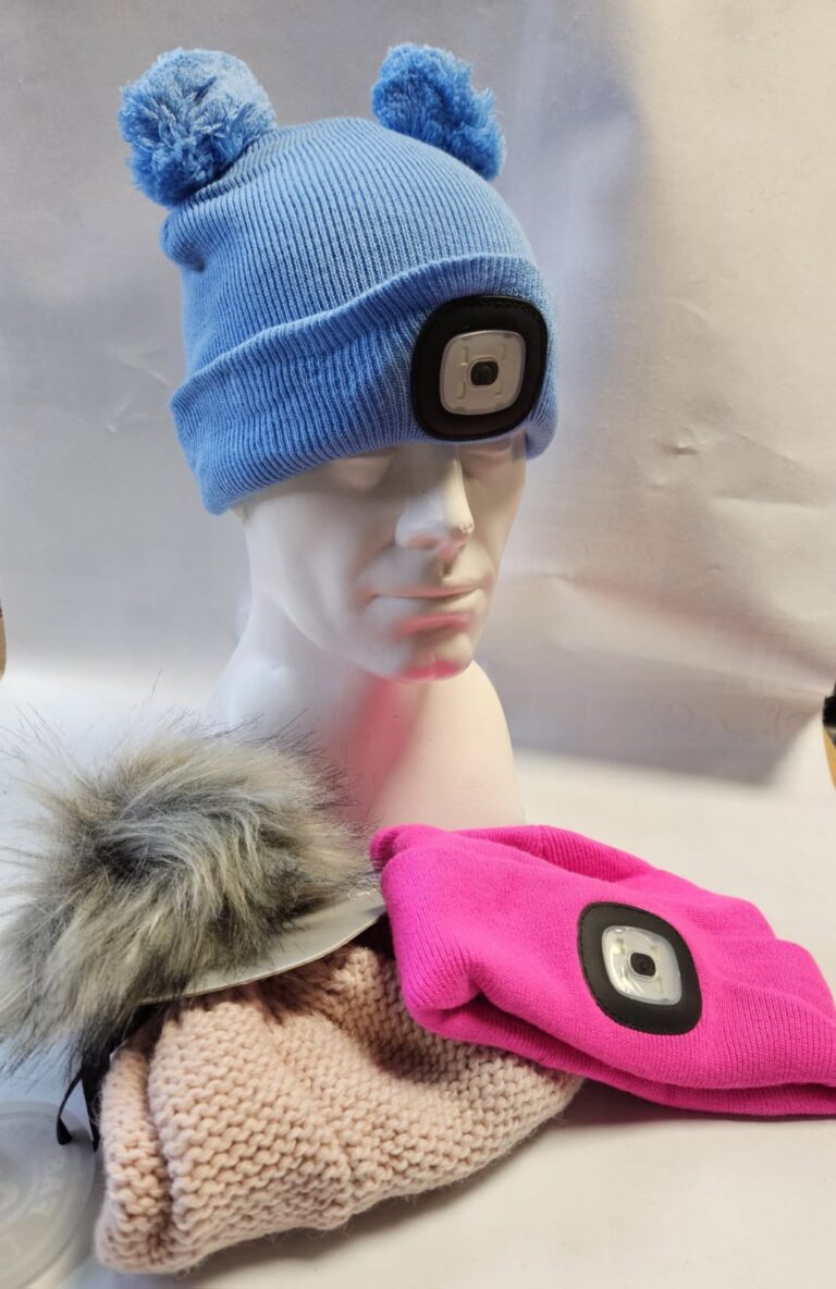 Obrázok zobrazuje tri zimné čiapky: svetlomodrú čiapku s pomponmi a LED svetlom, ružovú čiapku s LED svetlom a béžovú pletenú čiapku s kožušinovým detailom, umiestnené na buste.